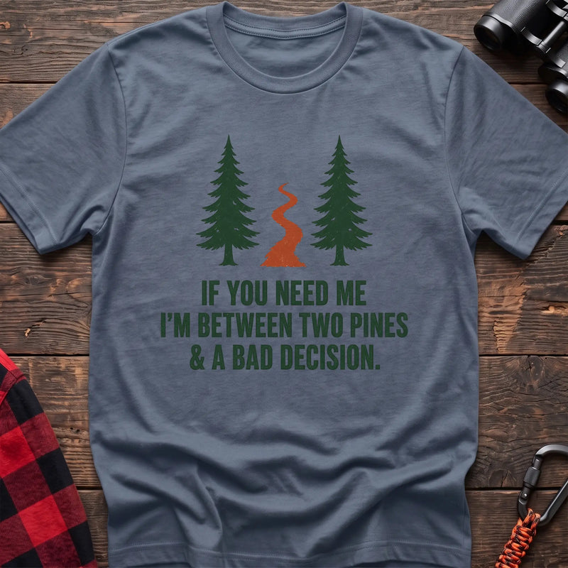 Stone blue cotton t-shirt with two pines and a trail graphic and If You Need Me I’m Between Two Pines and a Bad Decision text on rustic wood