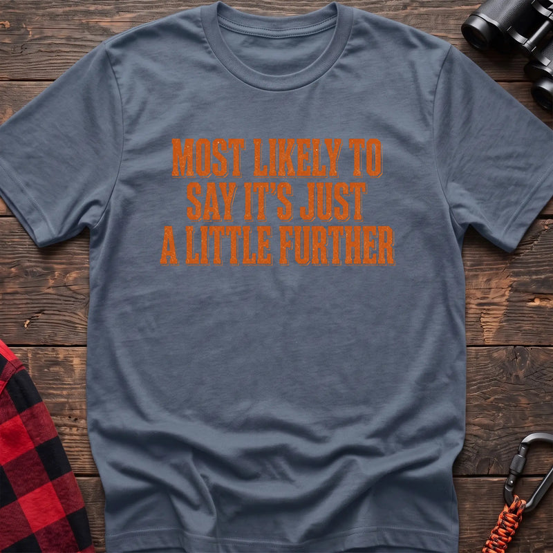 Stone blue cotton t-shirt with Most Likely to Say It’s Just a Little Further text on rustic wood