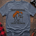 Stone blue t-shirt with a cartoon polar bear wearing a backpack and hat while holding a hiking stick, with the text “PROFESSIONAL TRAIL SLOWER,” laid flat on a wooden surface.