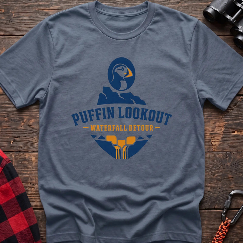 Stone blue cotton t-shirt with a puffin and waterfall graphic and Puffin Lookout Waterfall Detour text on rustic wood