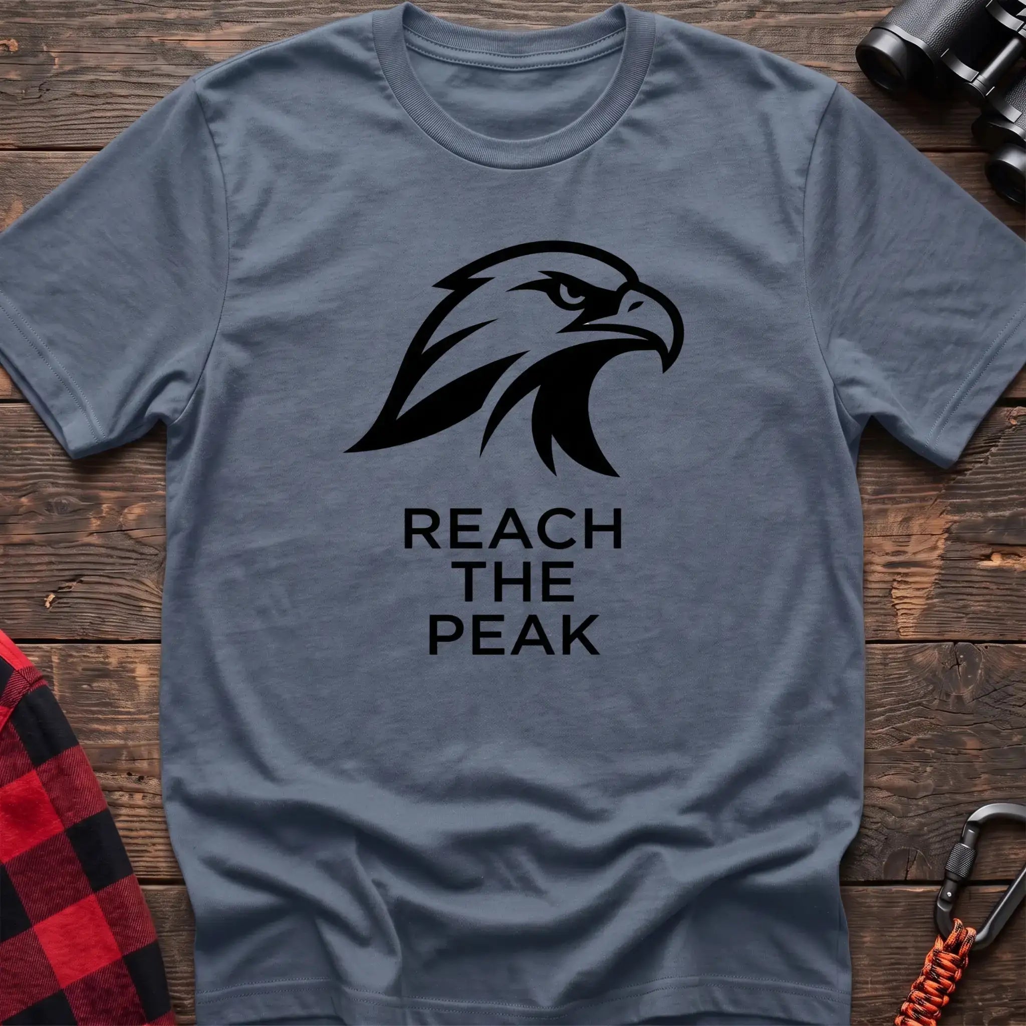 Stone blue crew-neck t-shirt with a black stylized eagle head logo and the text “REACH THE PEAK” printed on the front