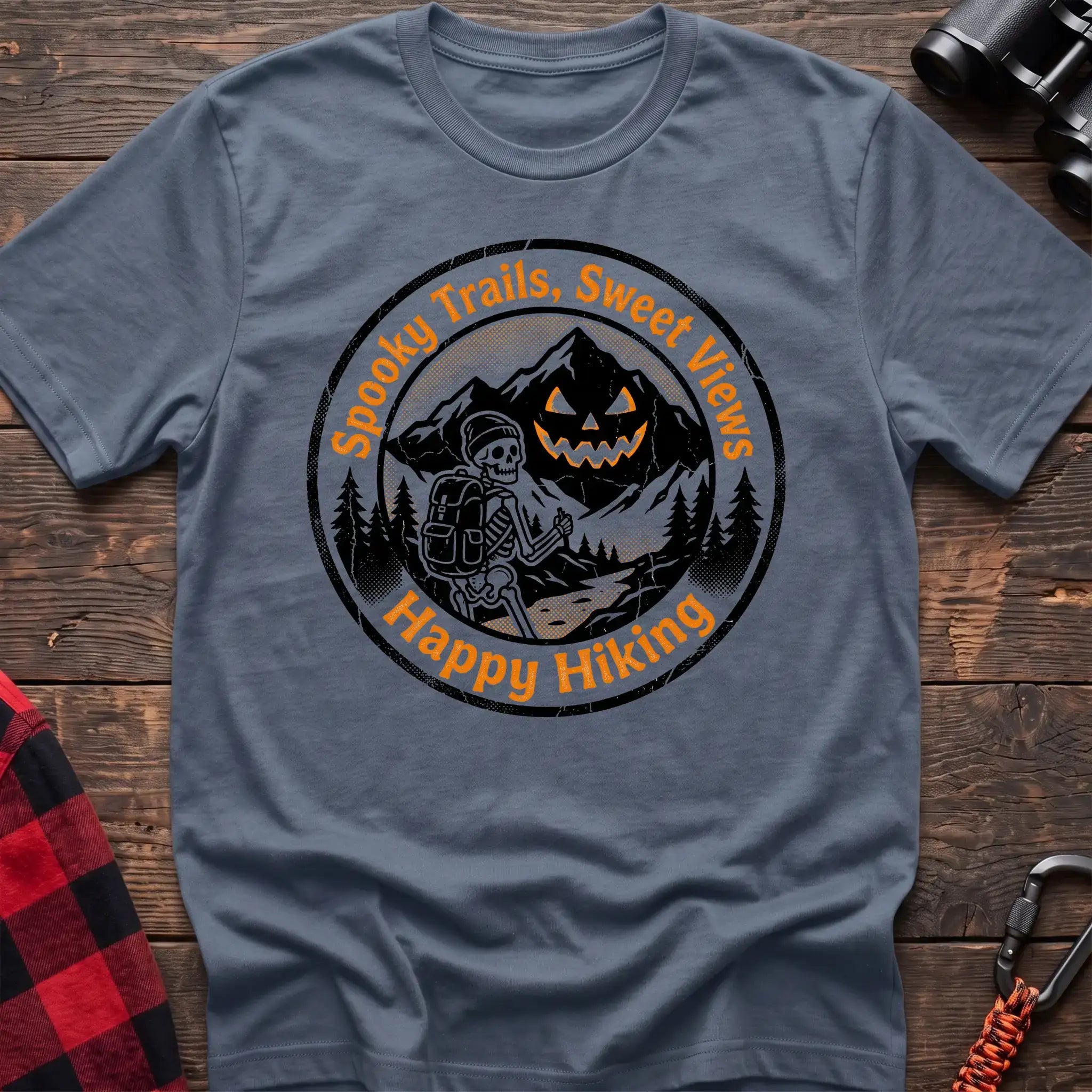 Stone blue t-shirt with circular graphic of a skeleton hiker giving a thumbs up in front of a jack-o-lantern mountain, reading Spooky Trails Sweet Views Happy Hiking