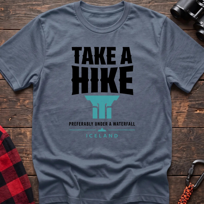 Stone blue cotton t-shirt with a waterfall graphic and Take a Hike Preferably Under a Waterfall Iceland text on rustic wood
