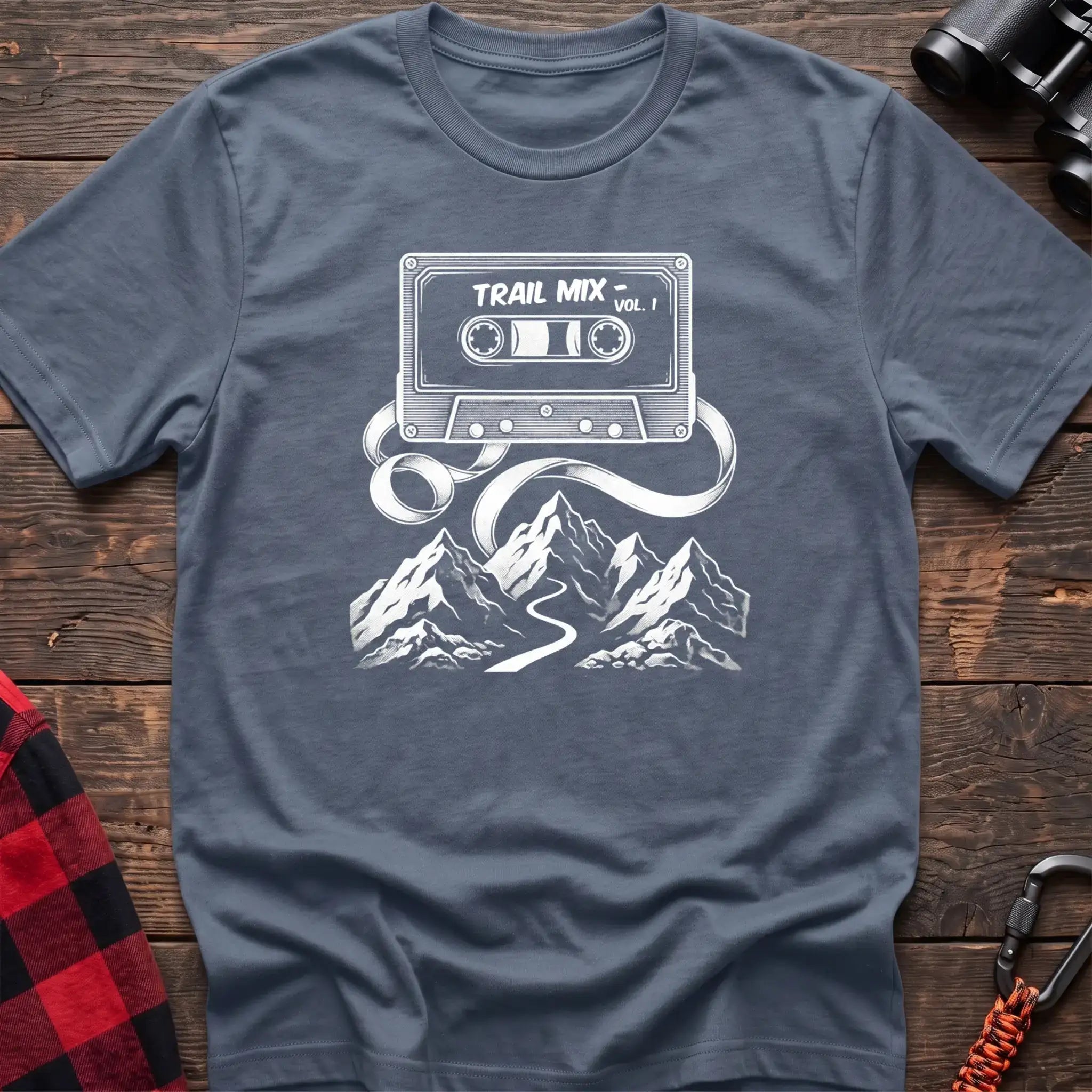 Stone blue t-shirt with white cassette tape graphic labeled Trail Mix Vol. 1, with tape unspooling into a trail through mountains