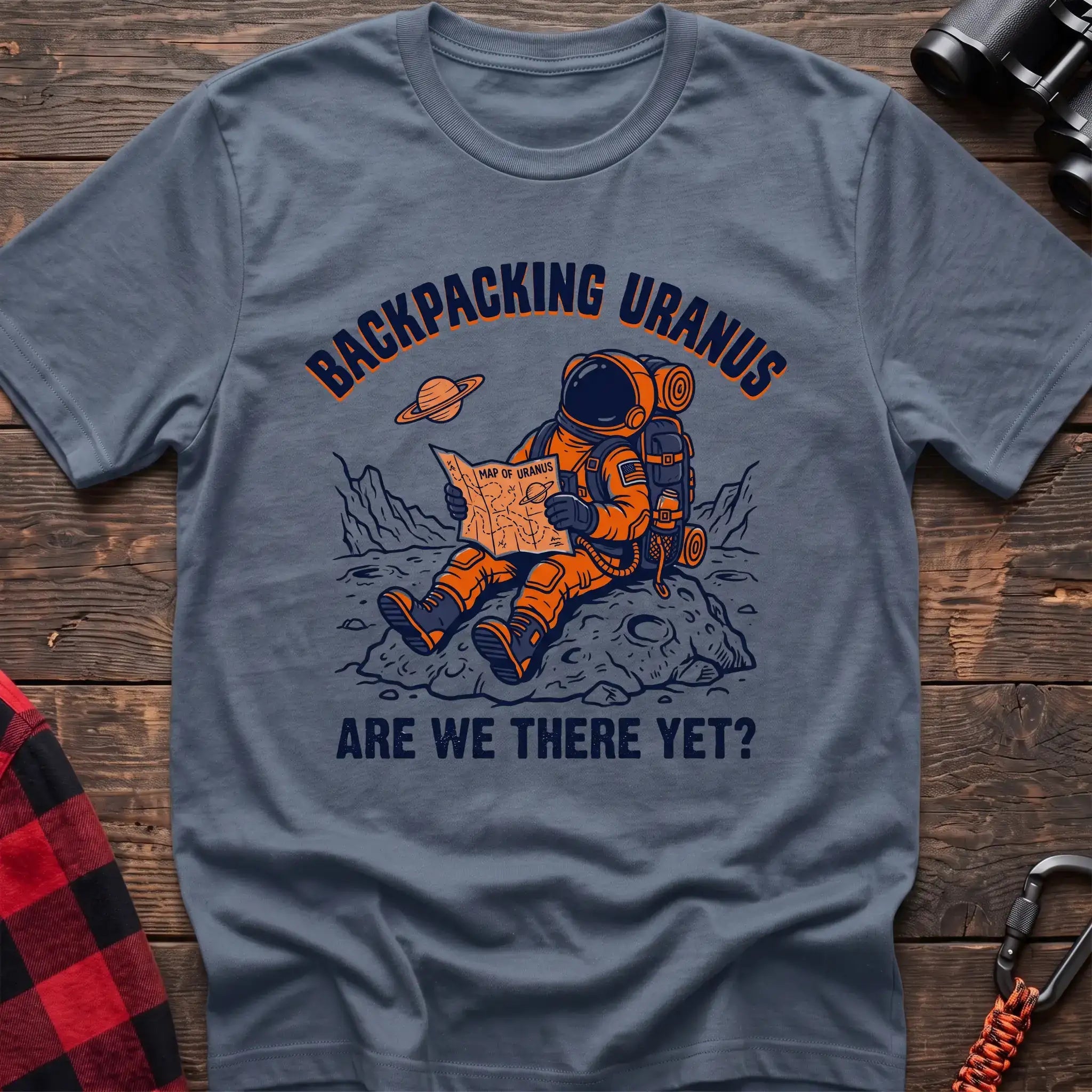 Stone blue t-shirt with astronaut sitting on a rock reading a Map of Uranus and the text Backpacking Uranus Are We There Yet