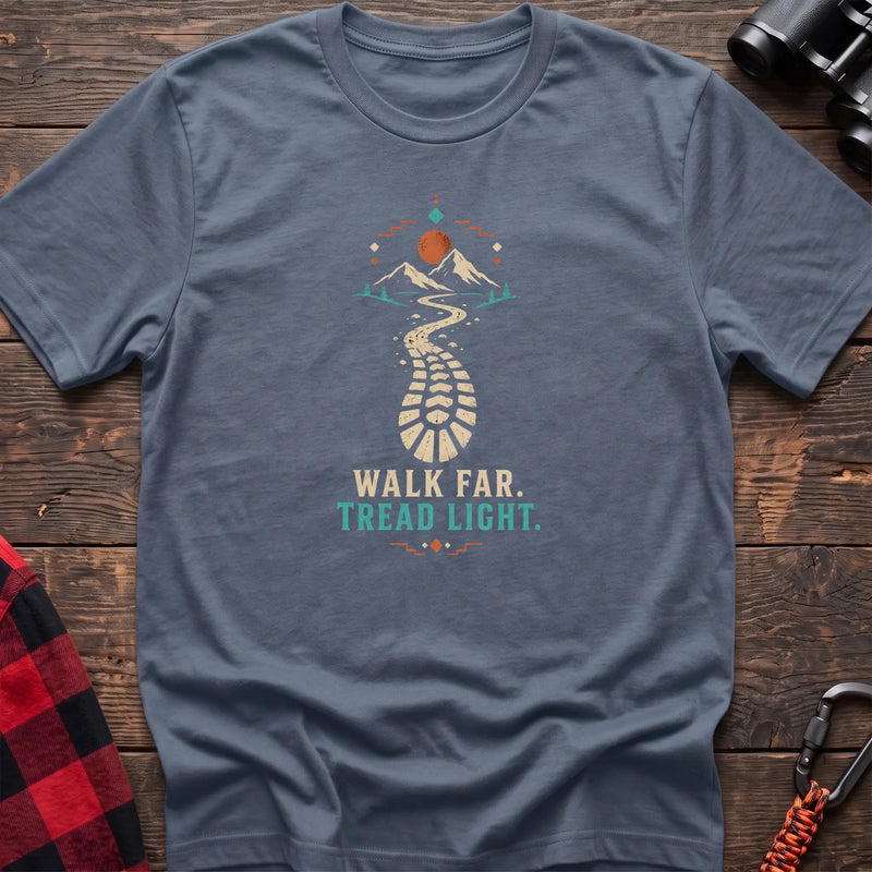 Stone blue cotton t-shirt with a bootprint trail and mountain graphic and Walk Far Tread Light text on rustic wood