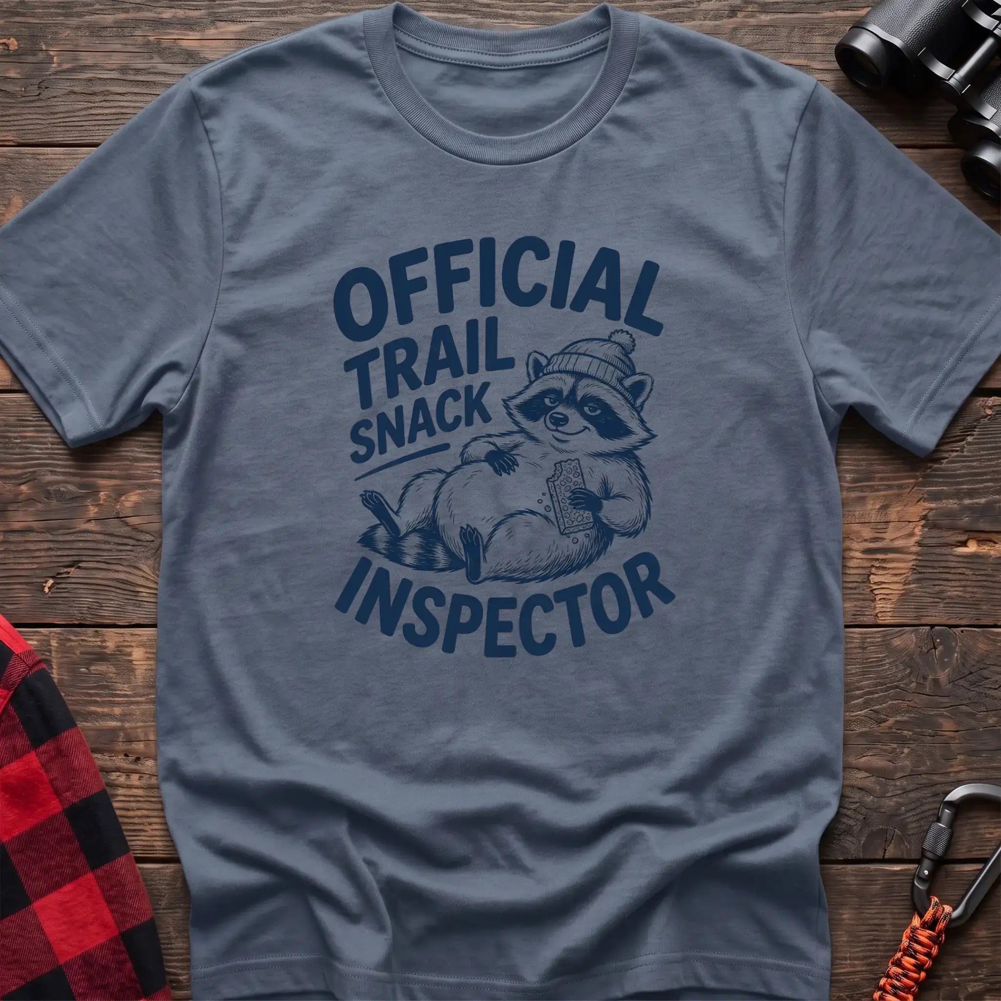 Stone blue t-shirt with cartoon raccoon holding a snack and the text Official Trail Snack Inspector