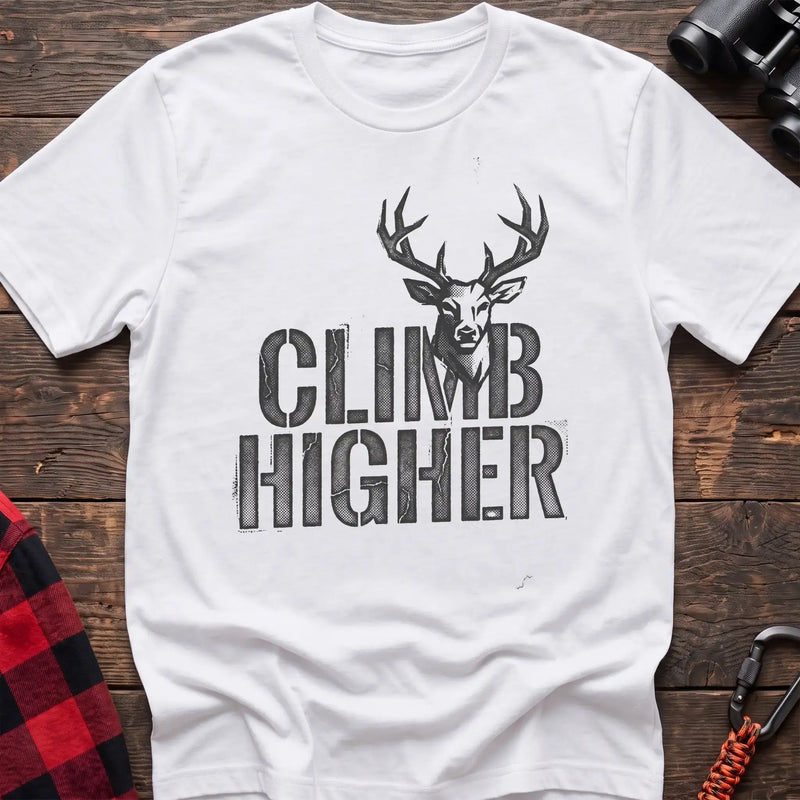 White t-shirt with a distressed dark graphic of a deer’s head and antlers rising from the bold text “CLIMB HIGHER,” laid flat on a wooden surface.