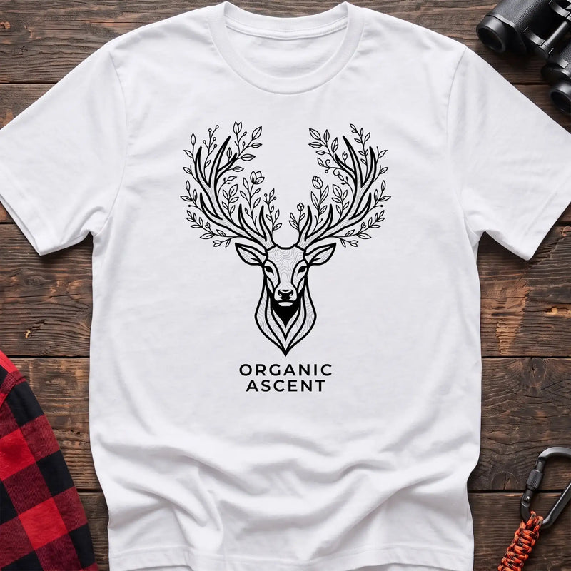 White t-shirt with a black line drawing of a deer’s head whose antlers are formed from leafy branches and flowers, with the text “ORGANIC ASCENT” printed below, laid flat on a wooden surface.