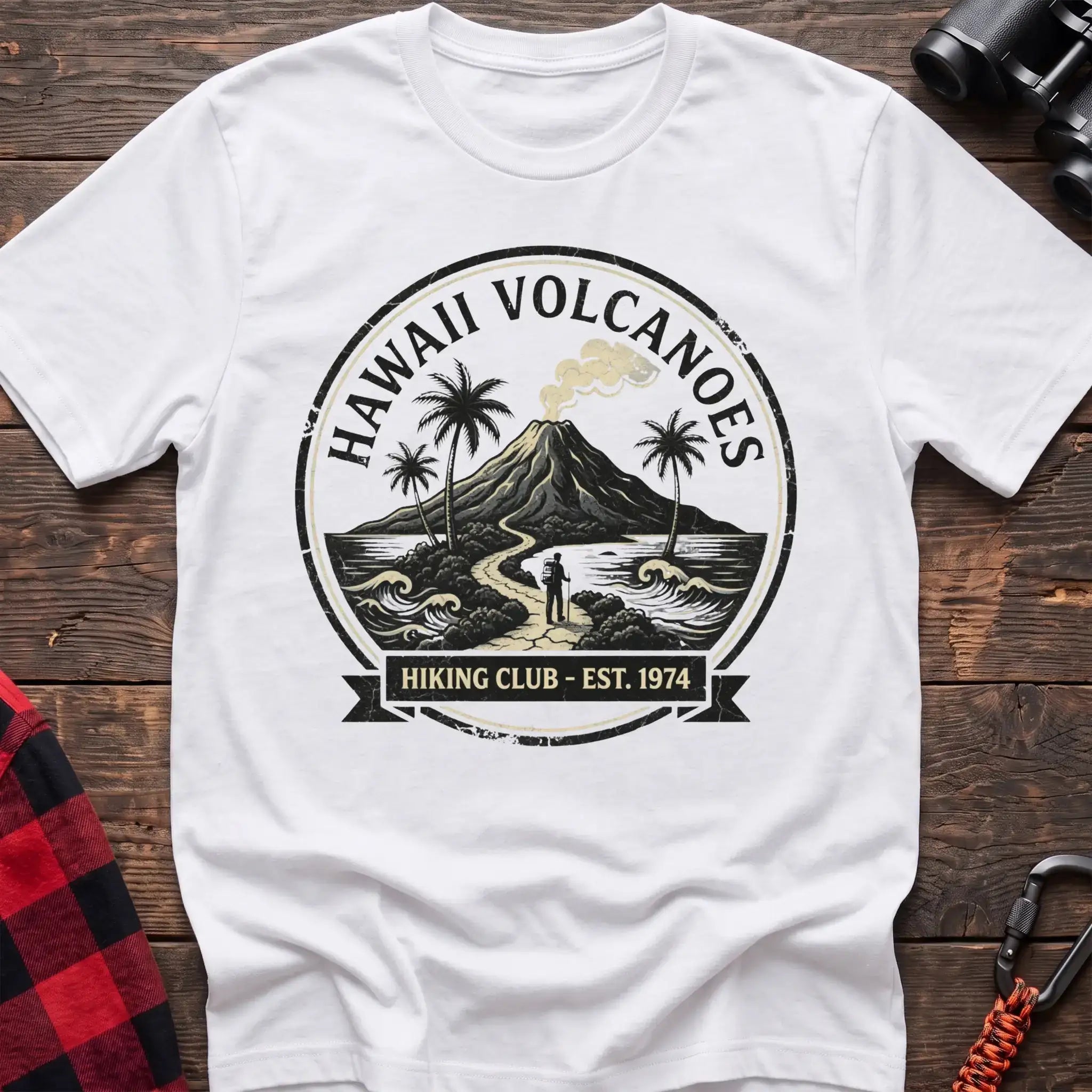White t-shirt with circular Hawaii Volcanoes badge graphic showing a volcano, palm trees, and a hiker, reading Hiking Club Est 1974