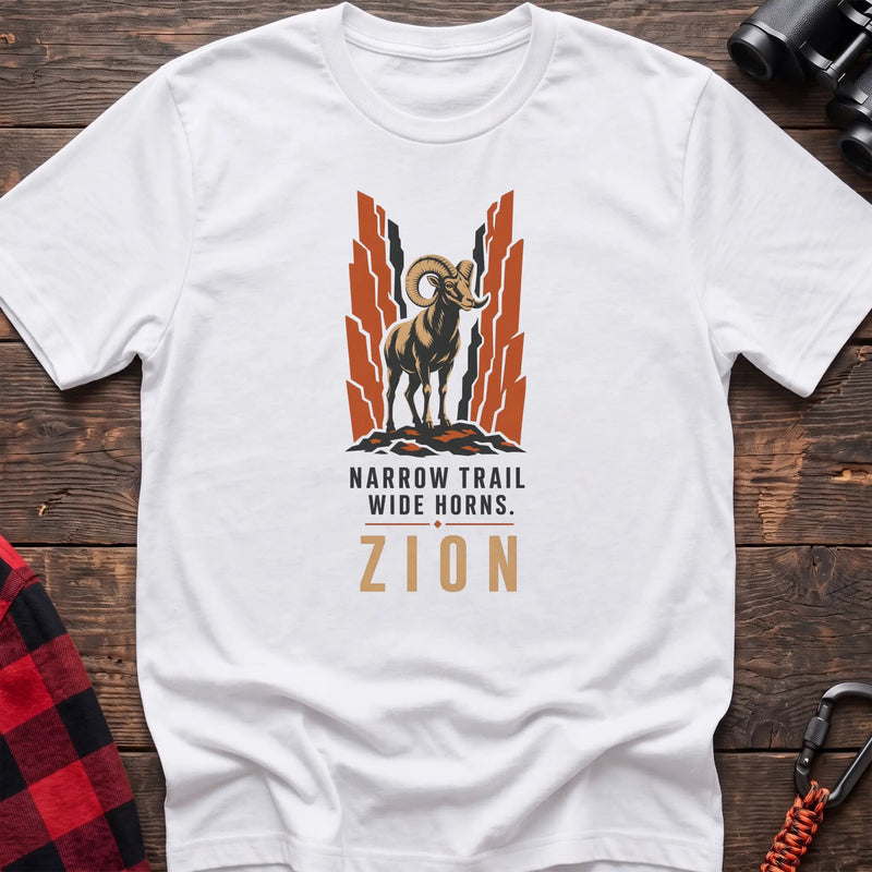 White cotton t-shirt with a bighorn sheep graphic and Narrow Trail Wide Horns Zion text on rustic wood