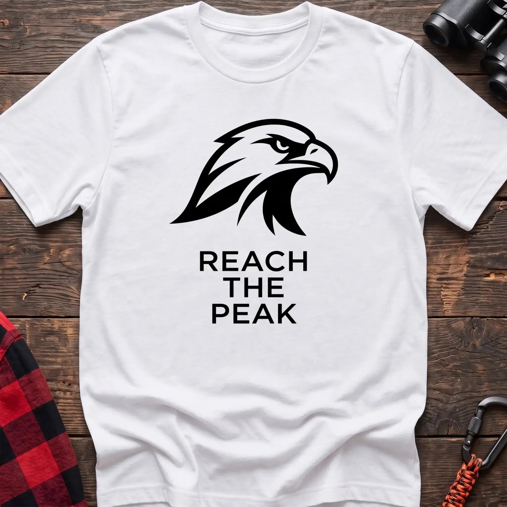 White crew-neck t-shirt with a black stylized eagle head logo and the text “REACH THE PEAK” printed on the front