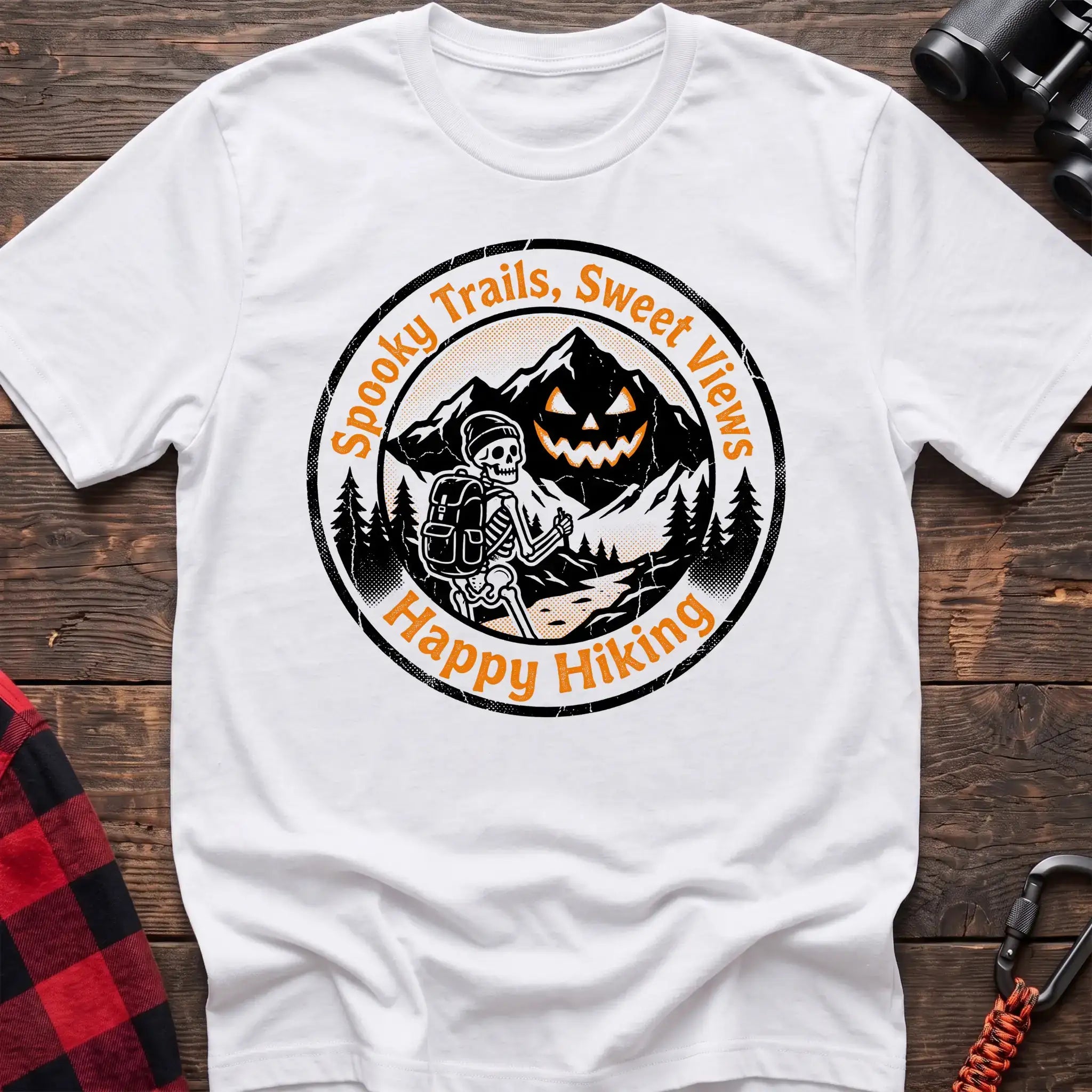 White t-shirt with circular graphic of a skeleton hiker giving a thumbs up in front of a jack-o-lantern mountain, reading Spooky Trails Sweet Views Happy Hiking