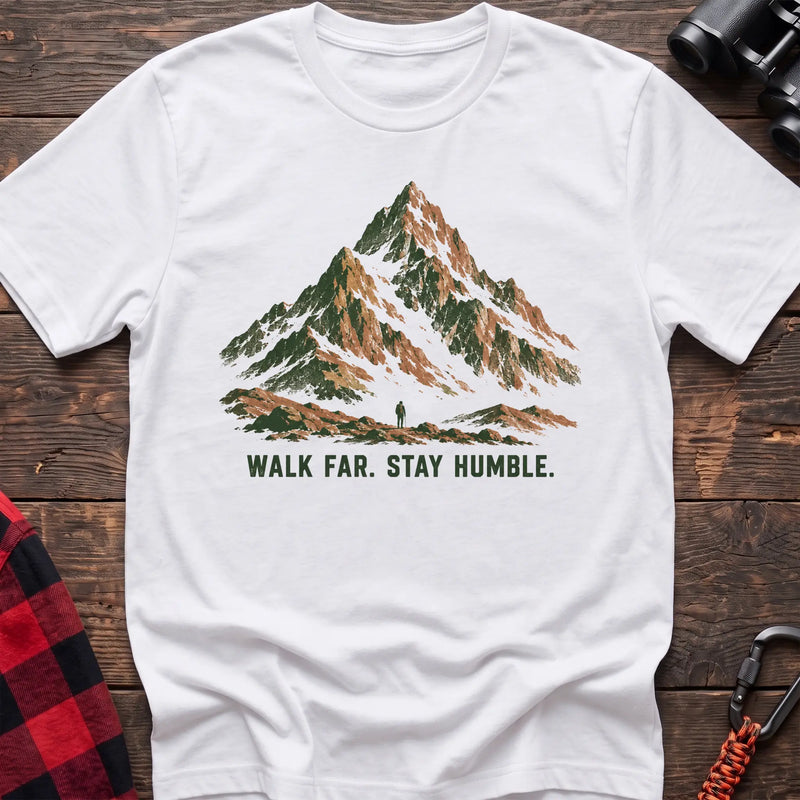 White cotton t-shirt with a mountain and hiker graphic and Walk Far Stay Humble text on rustic wood