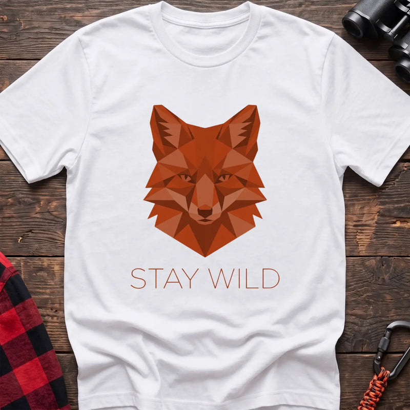 White t-shirt with a geometric low-poly orange fox head and the text “STAY WILD” printed below in matching orange, laid flat on a wooden surface.